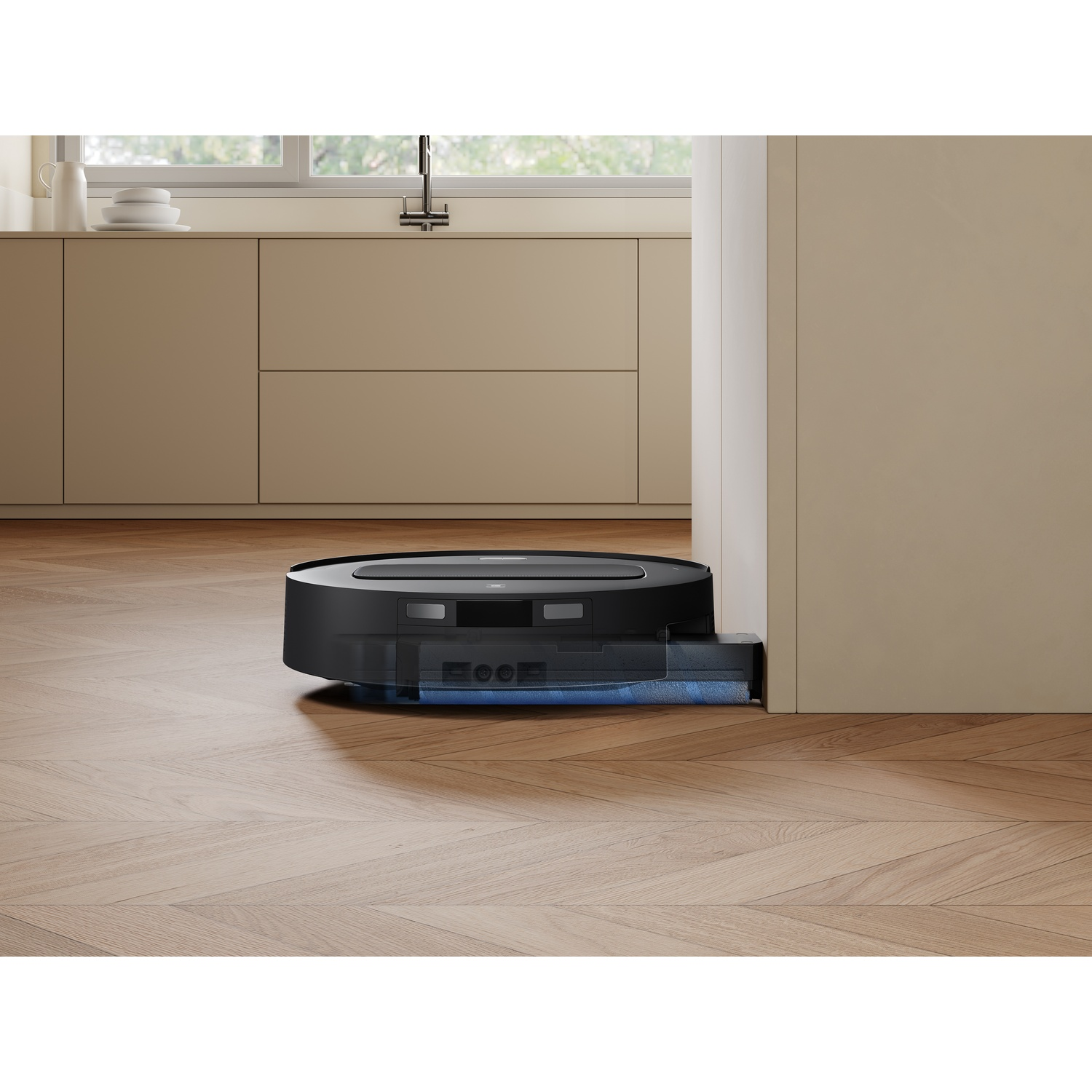 Un robot aspirapolvere nero pulisce il pavimento in legno di una cucina moderna.