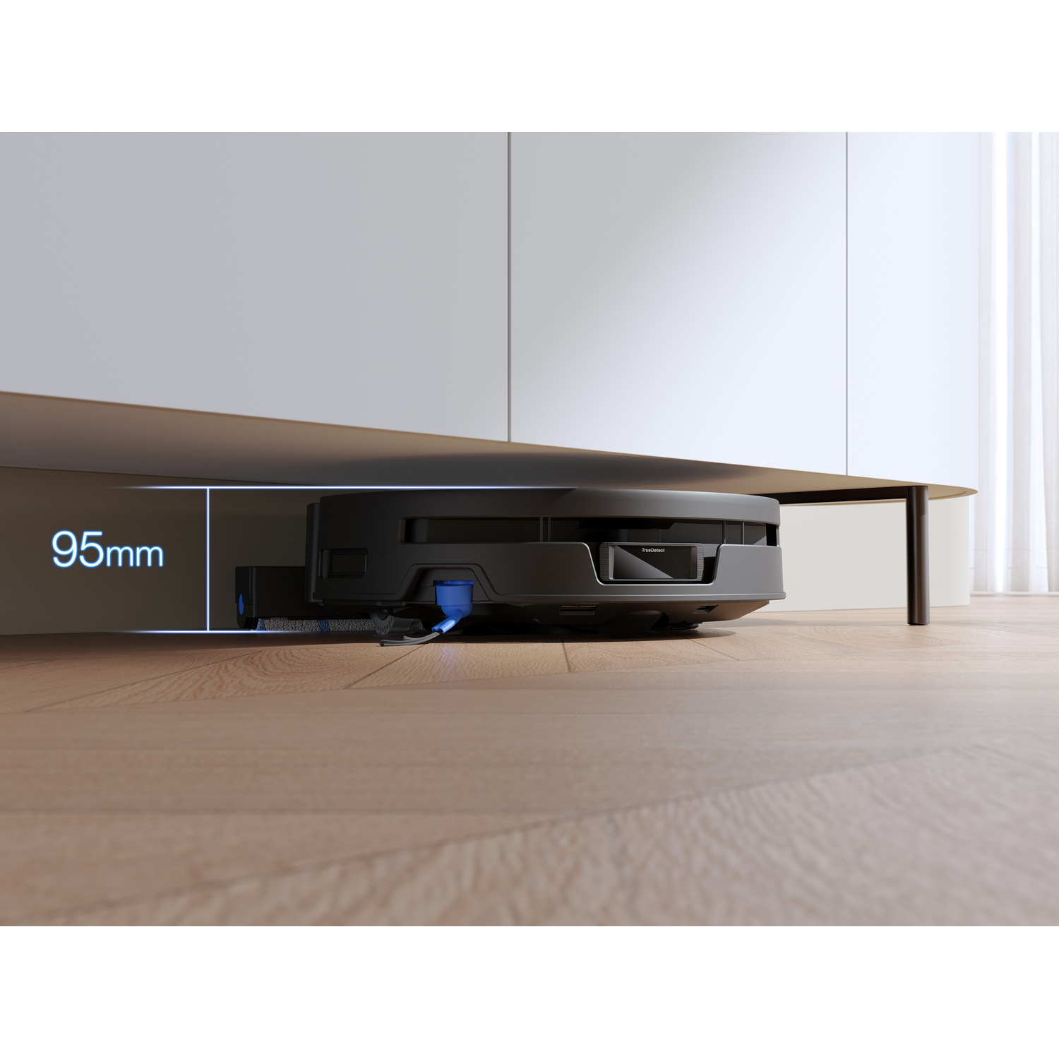 Un robot aspirapolvere nero pulisce il pavimento in legno sotto un mobile bianco con 95 mm di spazio.