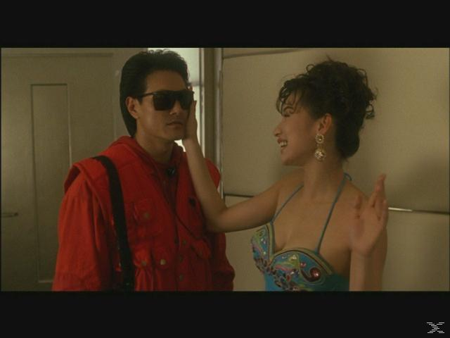 Ein Mann mit Sonnenbrille und roter Jacke steht drinnen, während eine Frau sein Gesicht berührt.