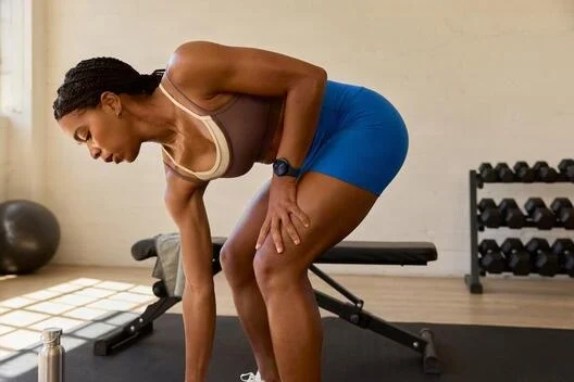 Una mujer con ropa deportiva está en un gimnasio, inclinándose hacia adelante.