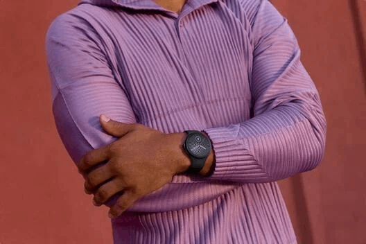 Una persona con suéter morado de canalé y reloj negro frente a un fondo rojo.