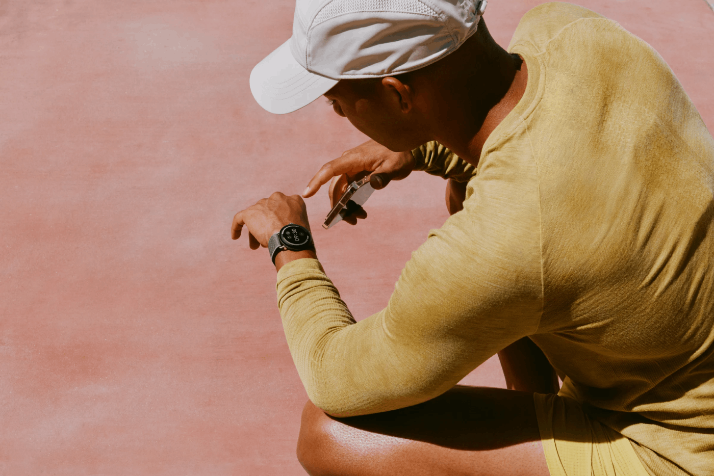 Un deportista con camiseta amarilla y gorra blanca mira su reloj inteligente.