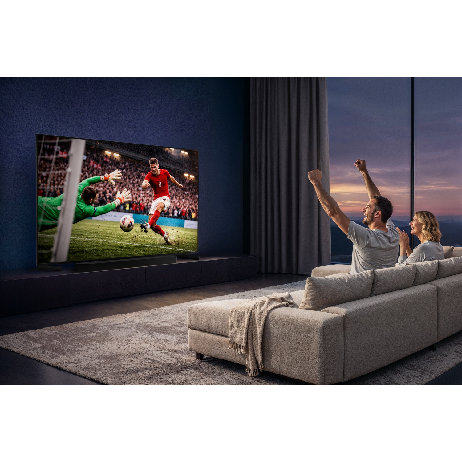 Een koppel zit op een bank in een moderne woonkamer en viert een voetbalwedstrijd op een groot televisiescherm.