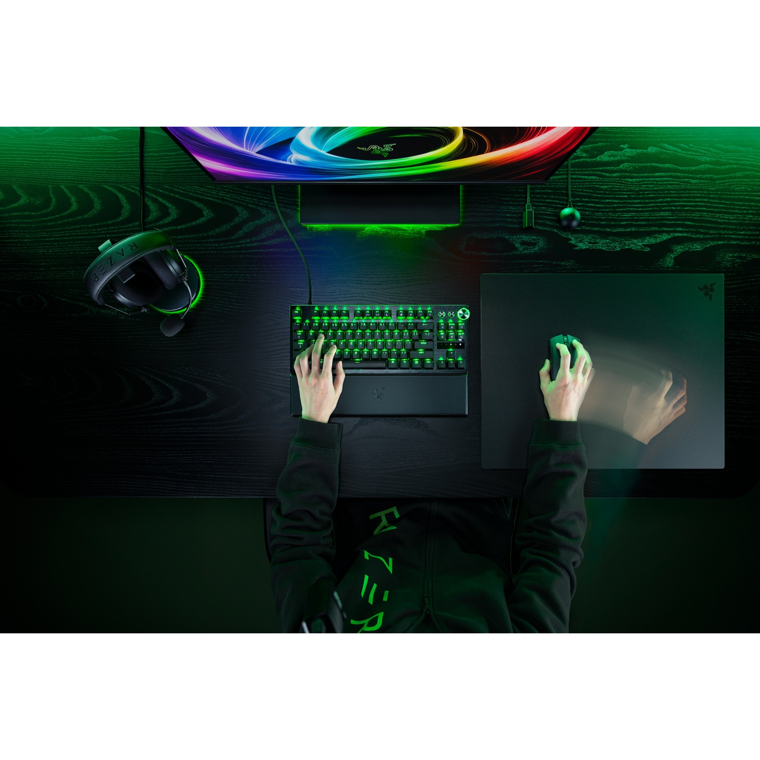 Vue de dessus d'un joueur à un bureau sombre utilisant clavier, souris et casque rétroéclairés vert.