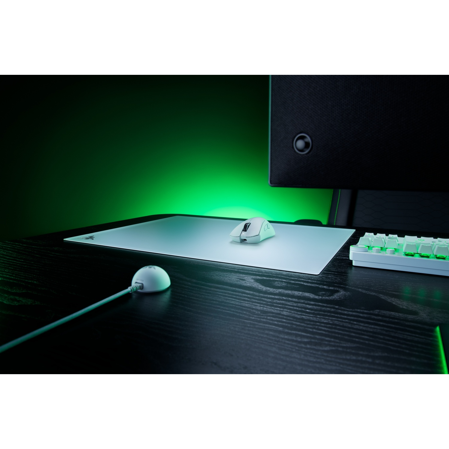 Une souris de jeu blanche sur un tapis de souris, illuminée par une lumière verte sur un bureau.
