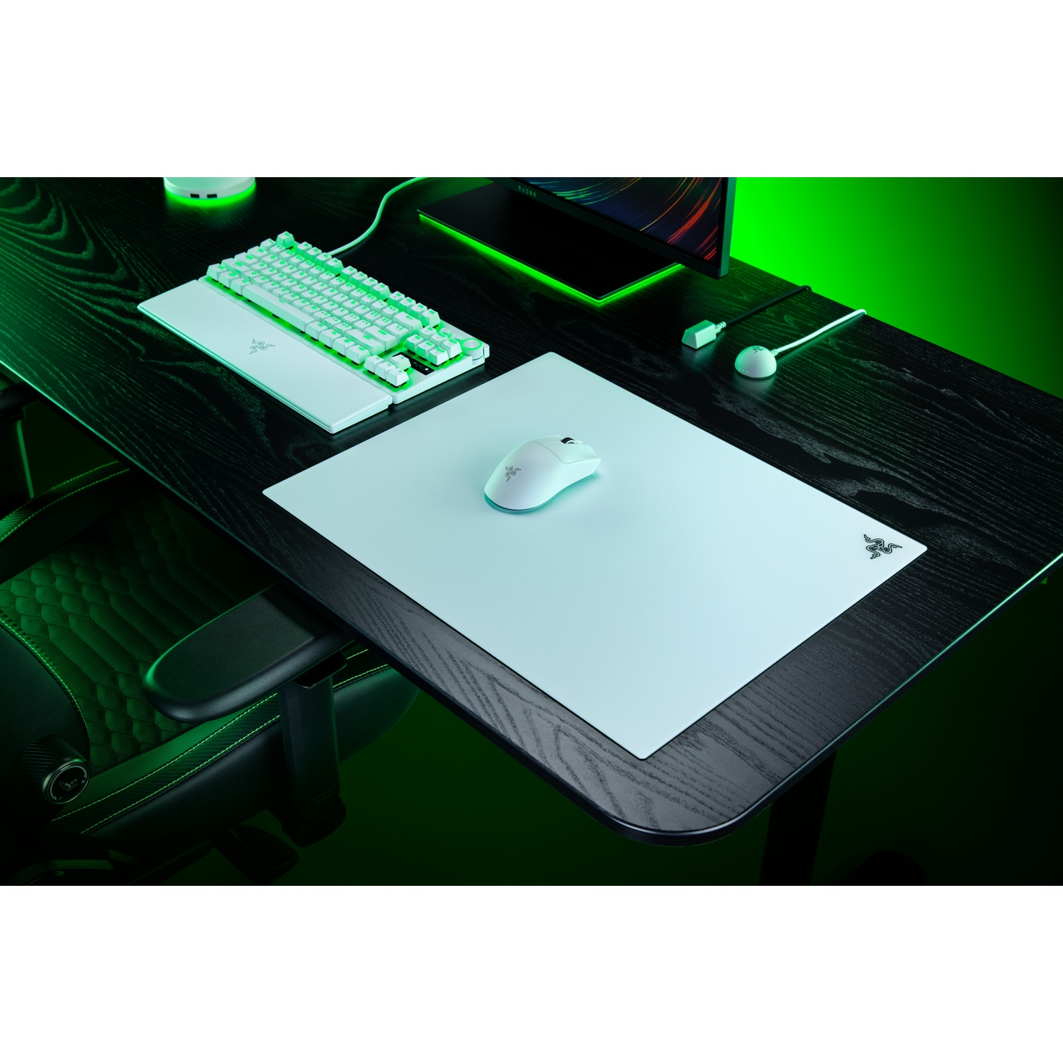Une configuration de jeu blanche avec clavier et souris sur un bureau en bois noir sur fond vert.