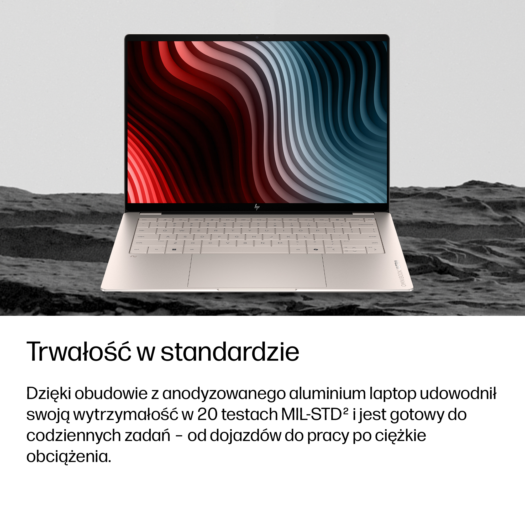 Otwarty laptop na kamienistym podłożu, z ekranem pokazującym czerwone i niebieskie fale.