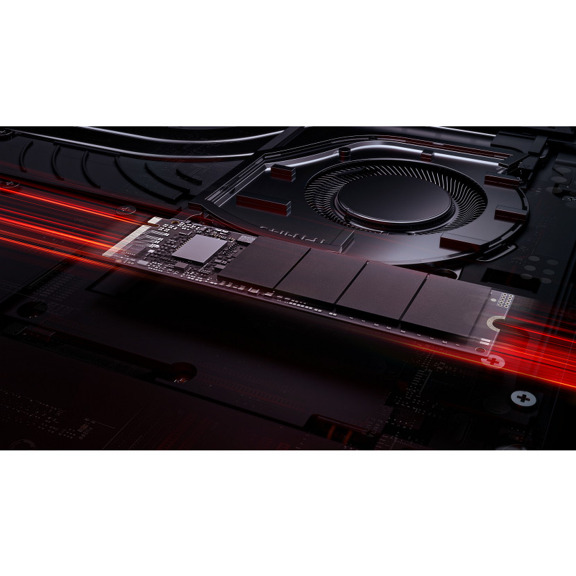 Dysk M.2 SSD leży na płycie głównej laptopa, z czerwonymi smugami światła i wentylatorem w tle.