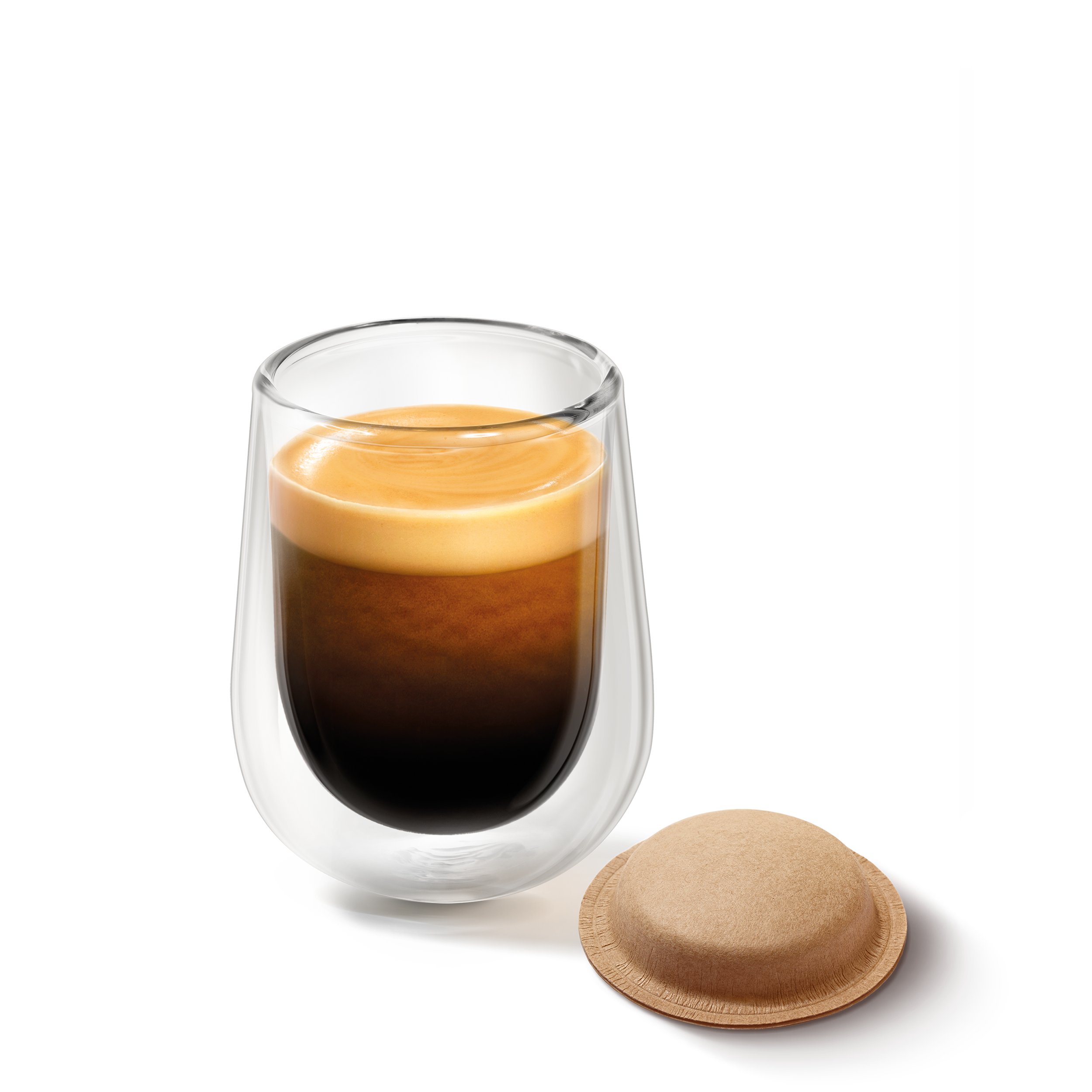 Ein doppelwandiges Glas mit frisch gebrühtem Kaffee und Crema, daneben ein Kaffeepad vor schwarzem Hintergrund.