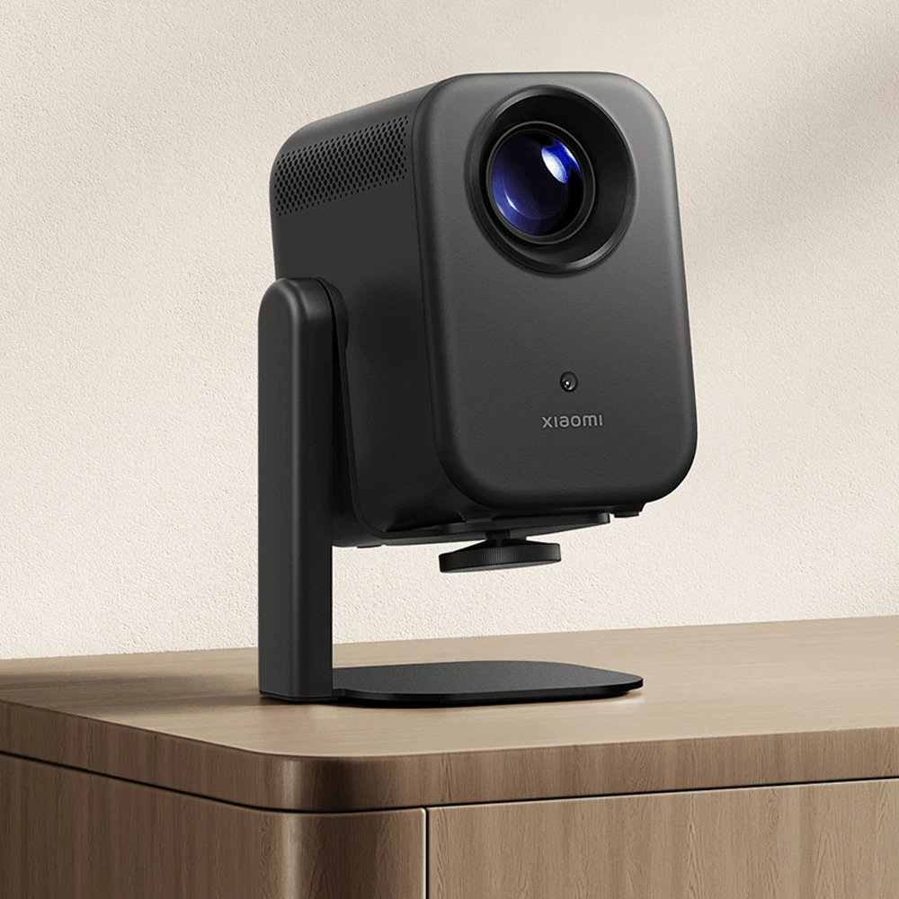 Un proiettore Xiaomi nero su supporto regolabile si trova su un mobile in legno chiaro.
