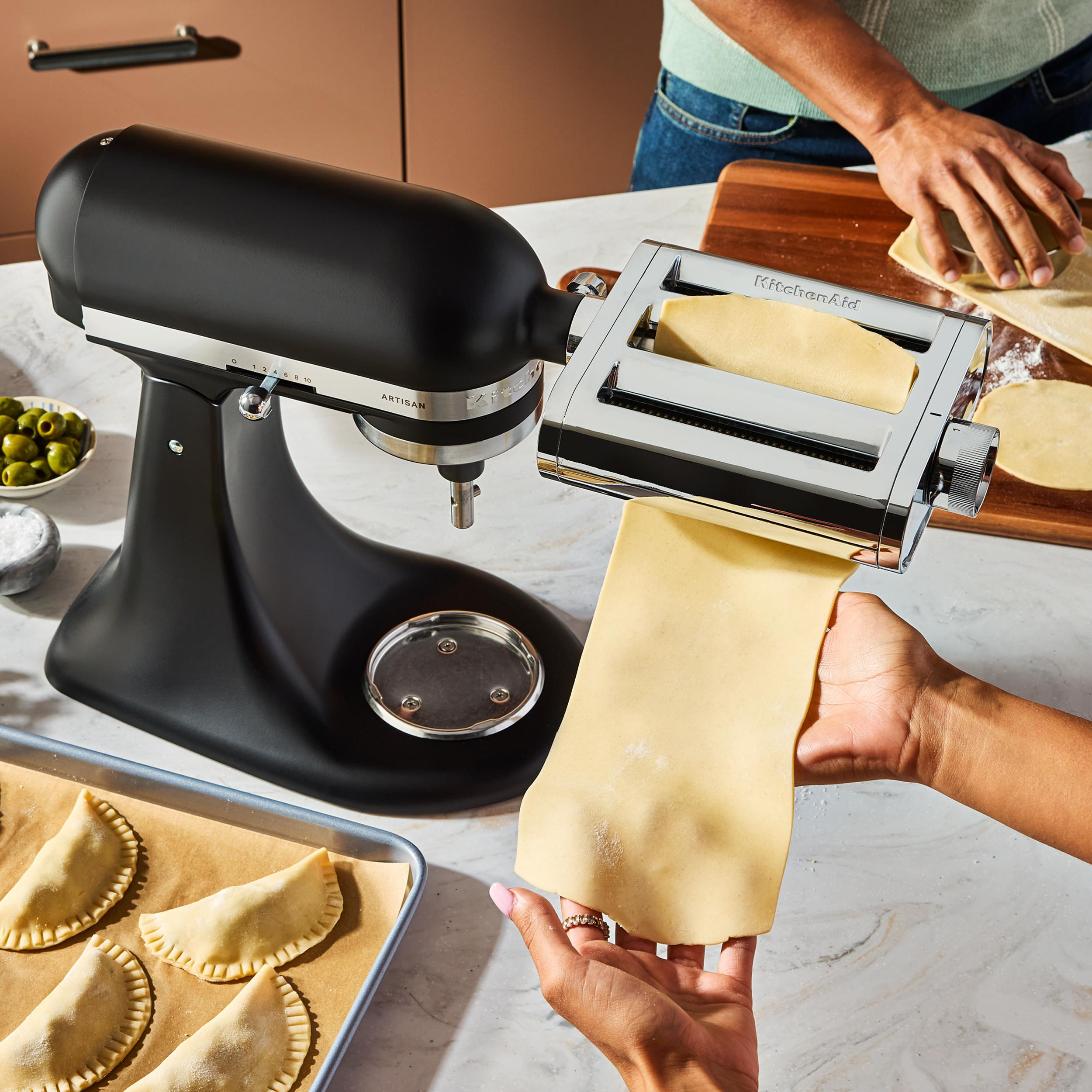 Schwarze Küchenmaschine mit Pastaaufsatz und Teig auf der Marmorarbeitsplatte.