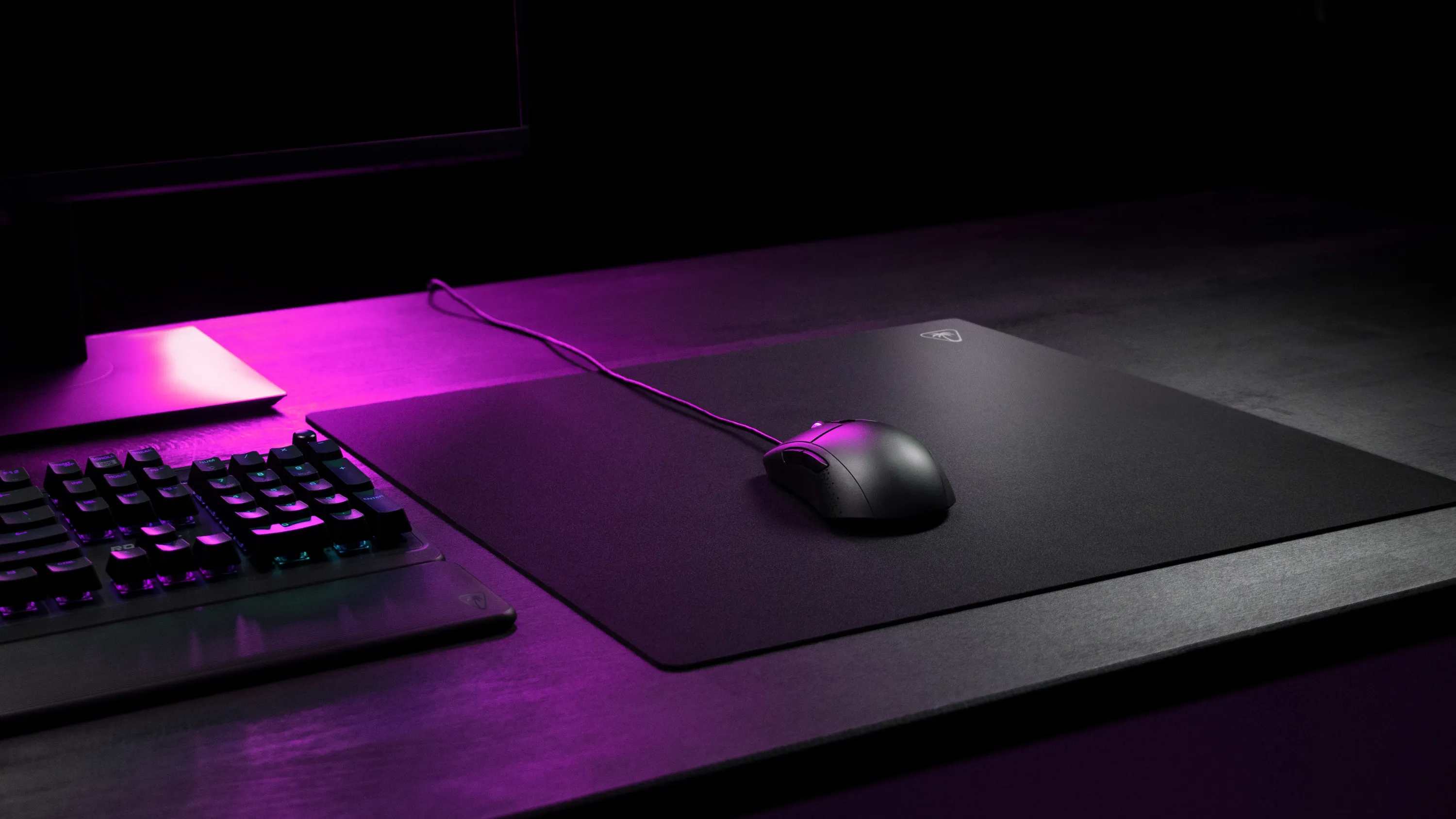 Une souris d'ordinateur noire repose sur un tapis, éclairée par une lumière violette.