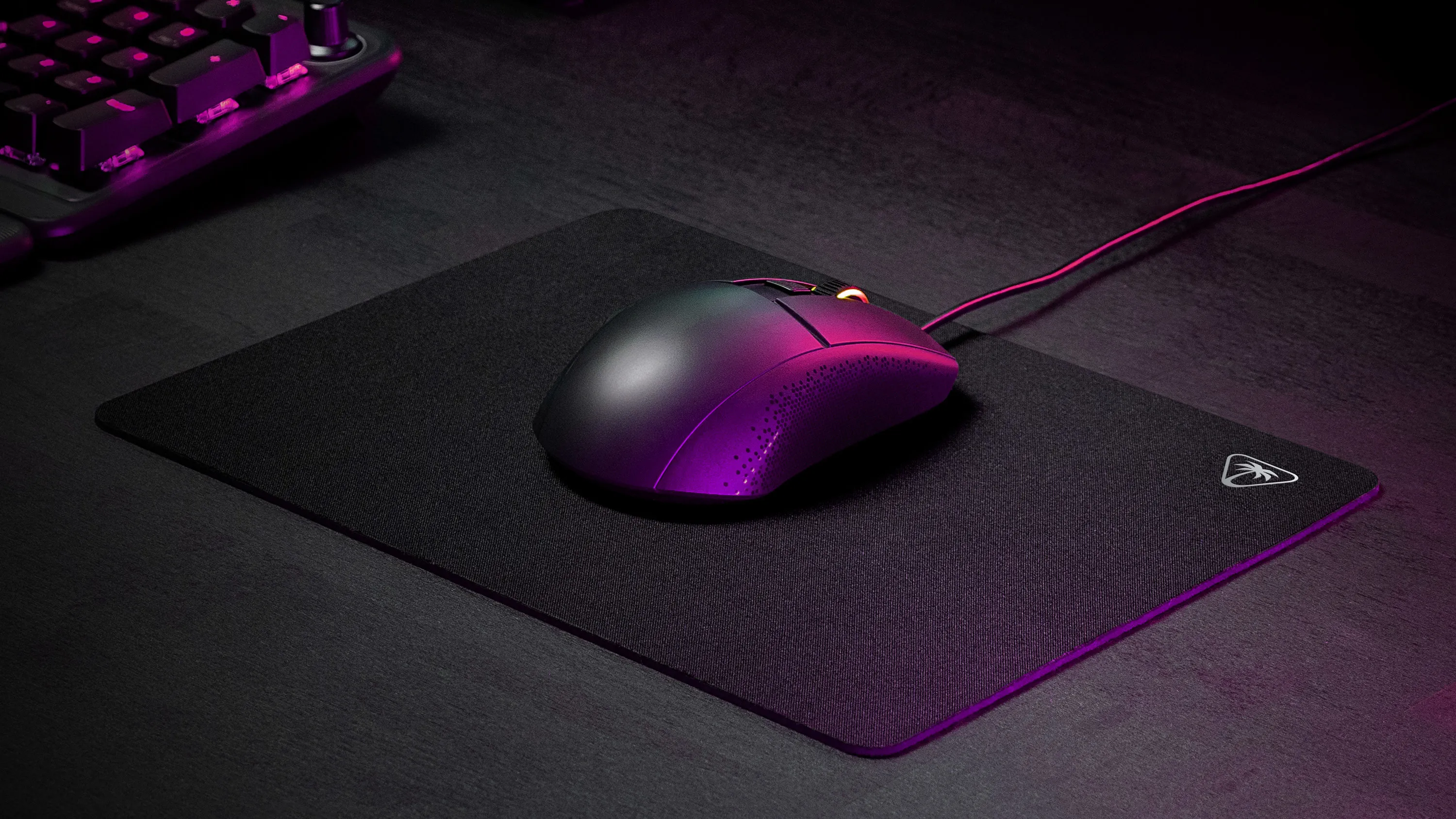 Une souris d'ordinateur noire à éclairage violet repose sur un tapis de souris à côté d'un clavier.