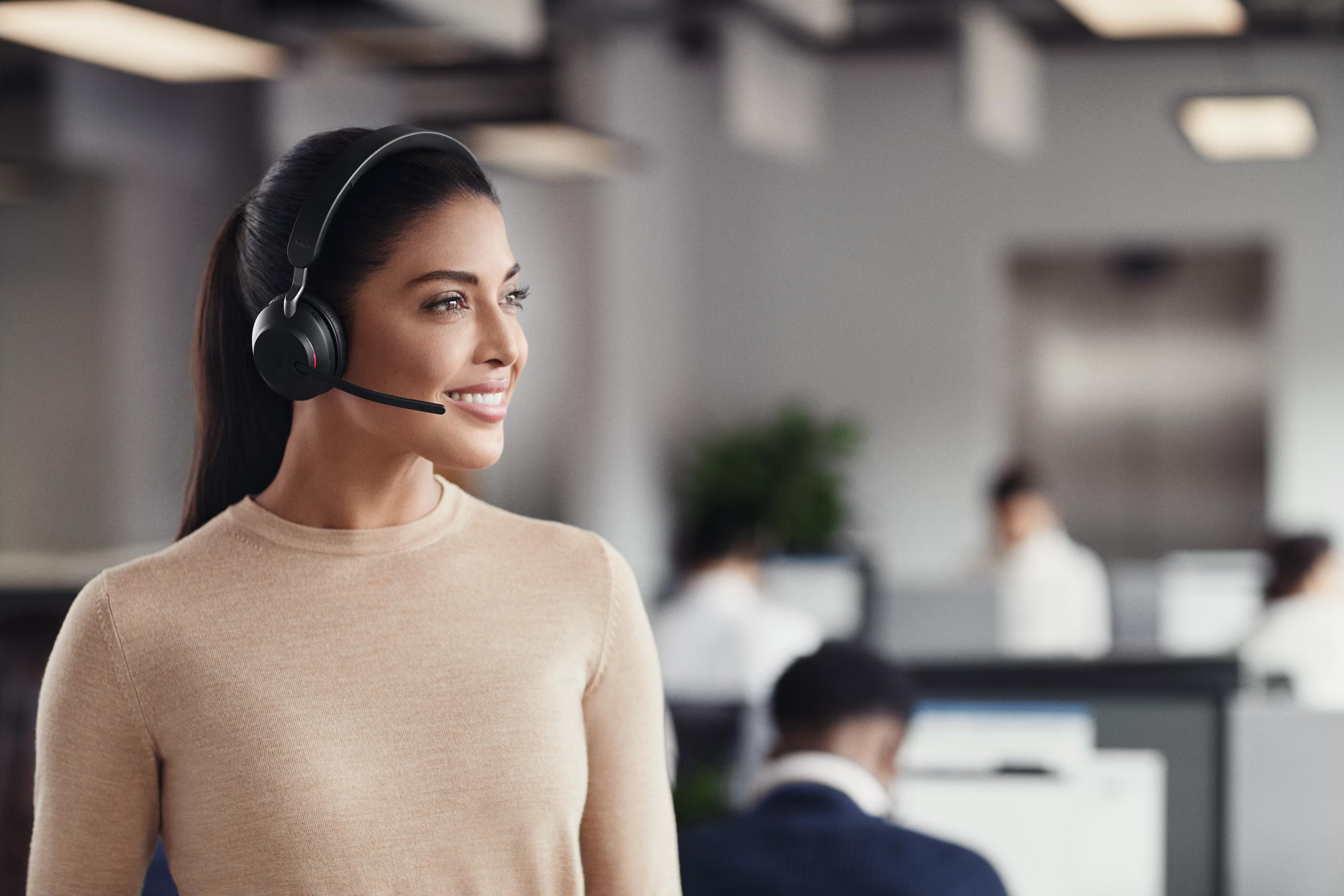 Una donna sorridente con le cuffie in un ufficio moderno e luminoso.