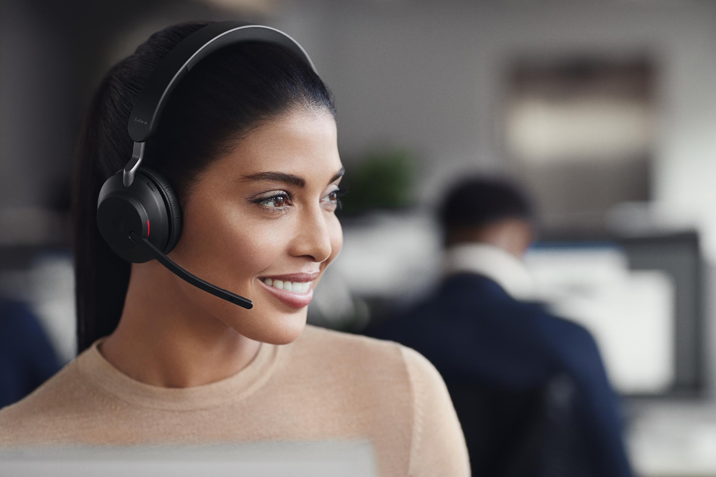 Una donna sorridente indossa cuffie nere con microfono in un ufficio.