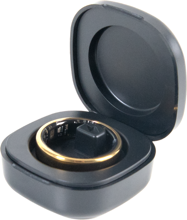 Une bague connectée dorée repose dans un boîtier de charge noir ouvert sur fond noir.