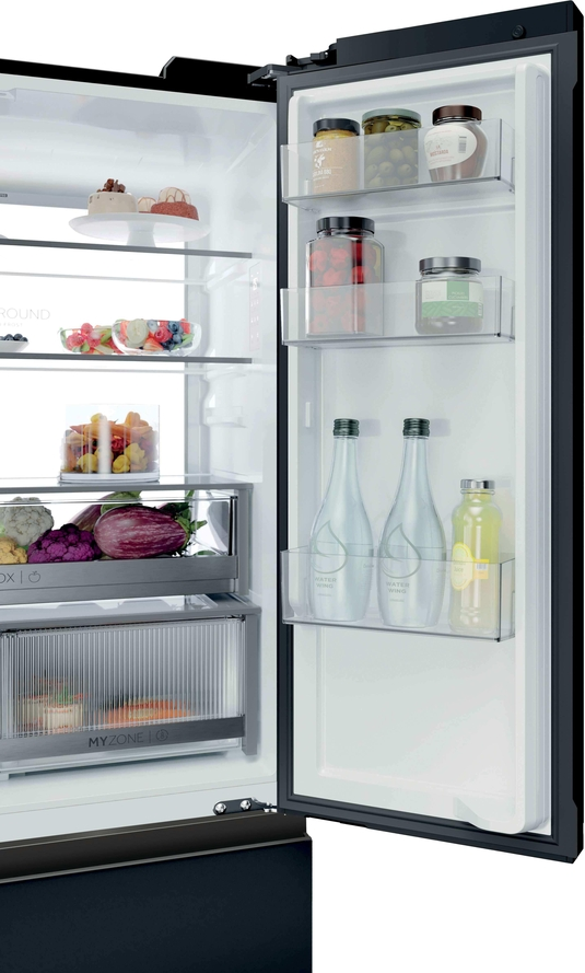 Ein offener, schwarzer Kühlschrank gefüllt mit Gemüse, Früchten, Gläsern und Flaschen auf den Regalen und in der Tür.