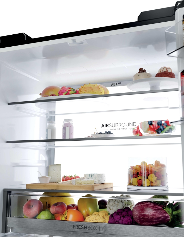 Ein offener Kühlschrank mit frischen Lebensmitteln wie Obst, Gemüse, Käse und Desserts auf mehreren Ebenen.