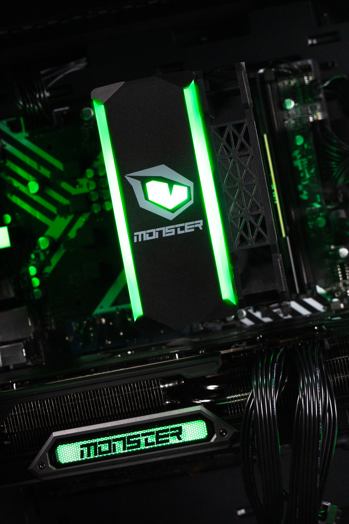 Siyah anakart üzerinde yeşil yanan Monster işlemci soğutucusu ve ekran kartı logosu olan oyuncu PC'sinin içi.