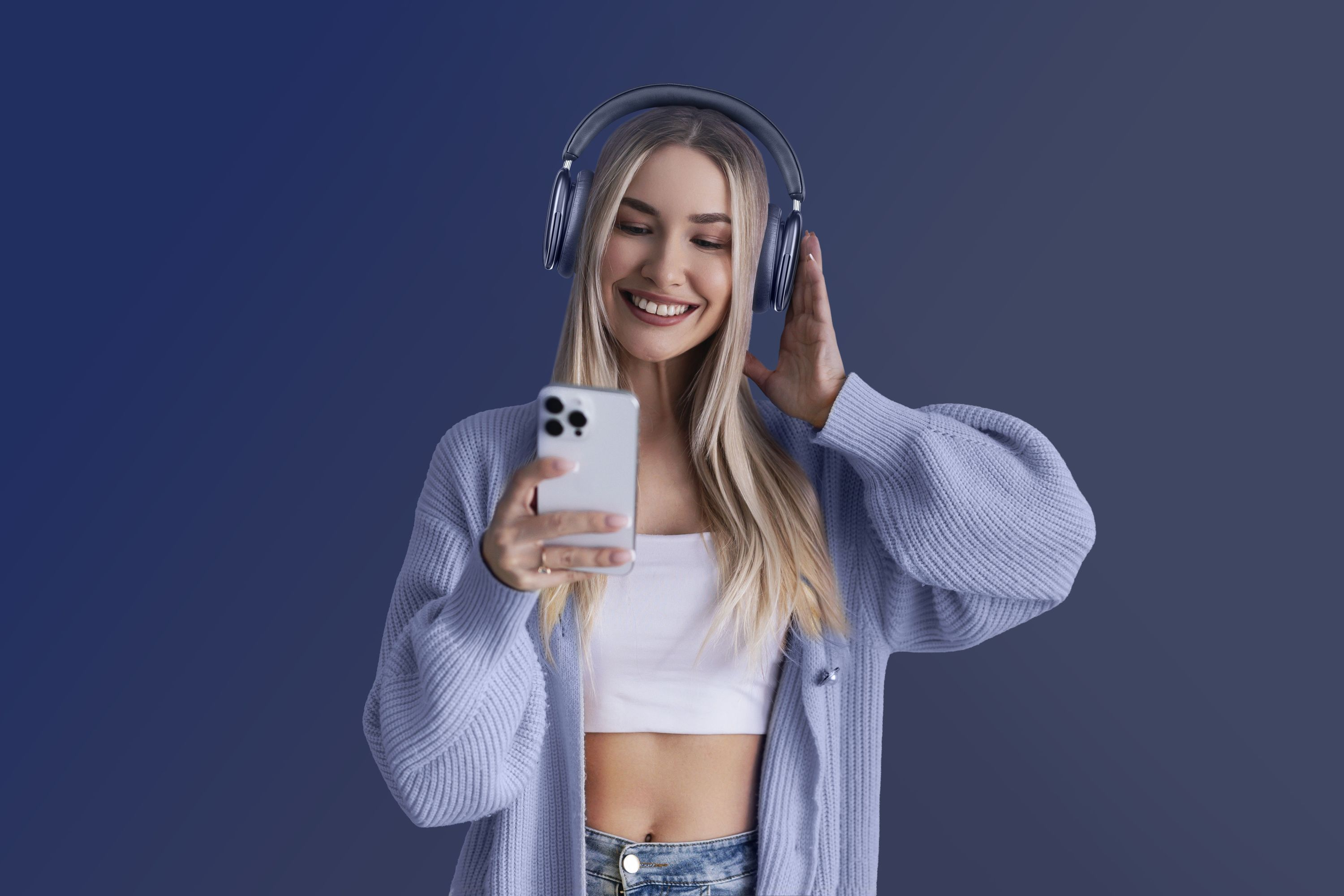 Kulaklık takan sarışın bir kadın, mavi arka planda akıllı telefon kullanırken gülümsüyor.