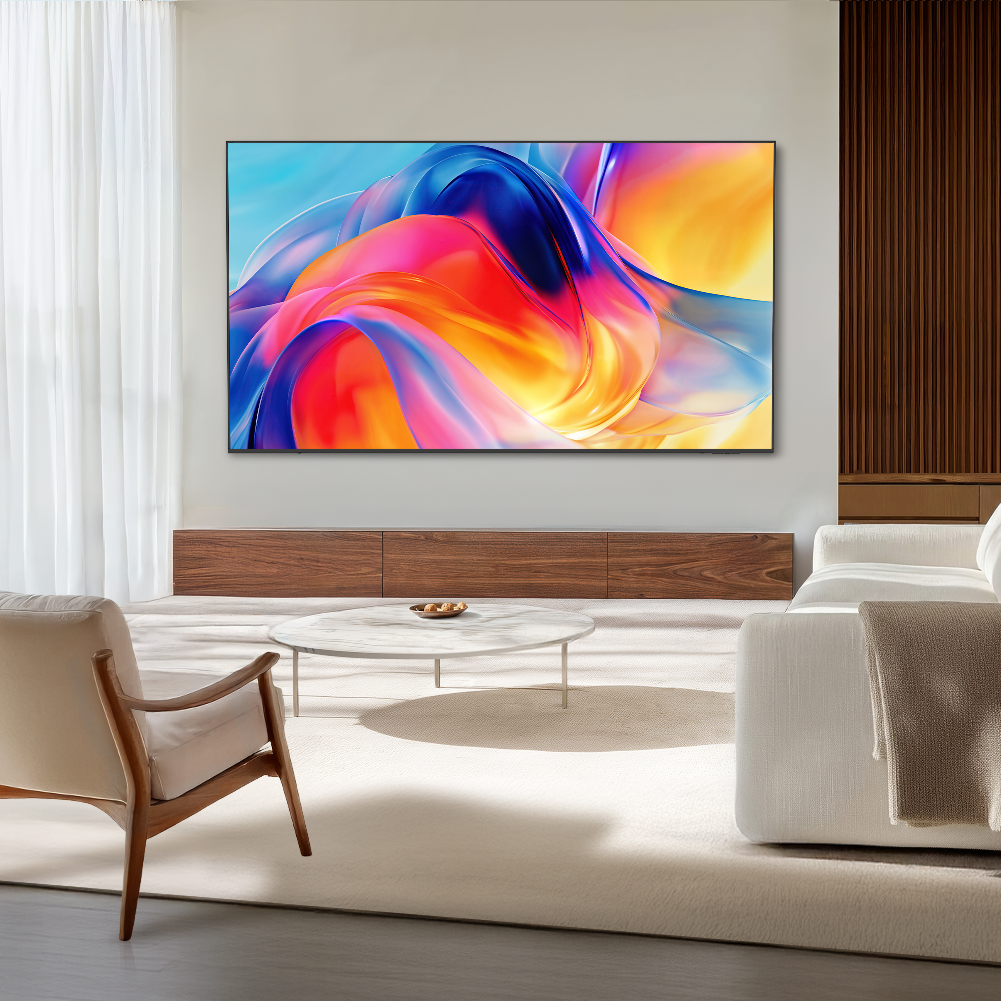 Wohnzimmer mit großem Fernseher, der eine bunte Grafik zeigt, weißer Couch und Holztisch vor heller Wand.