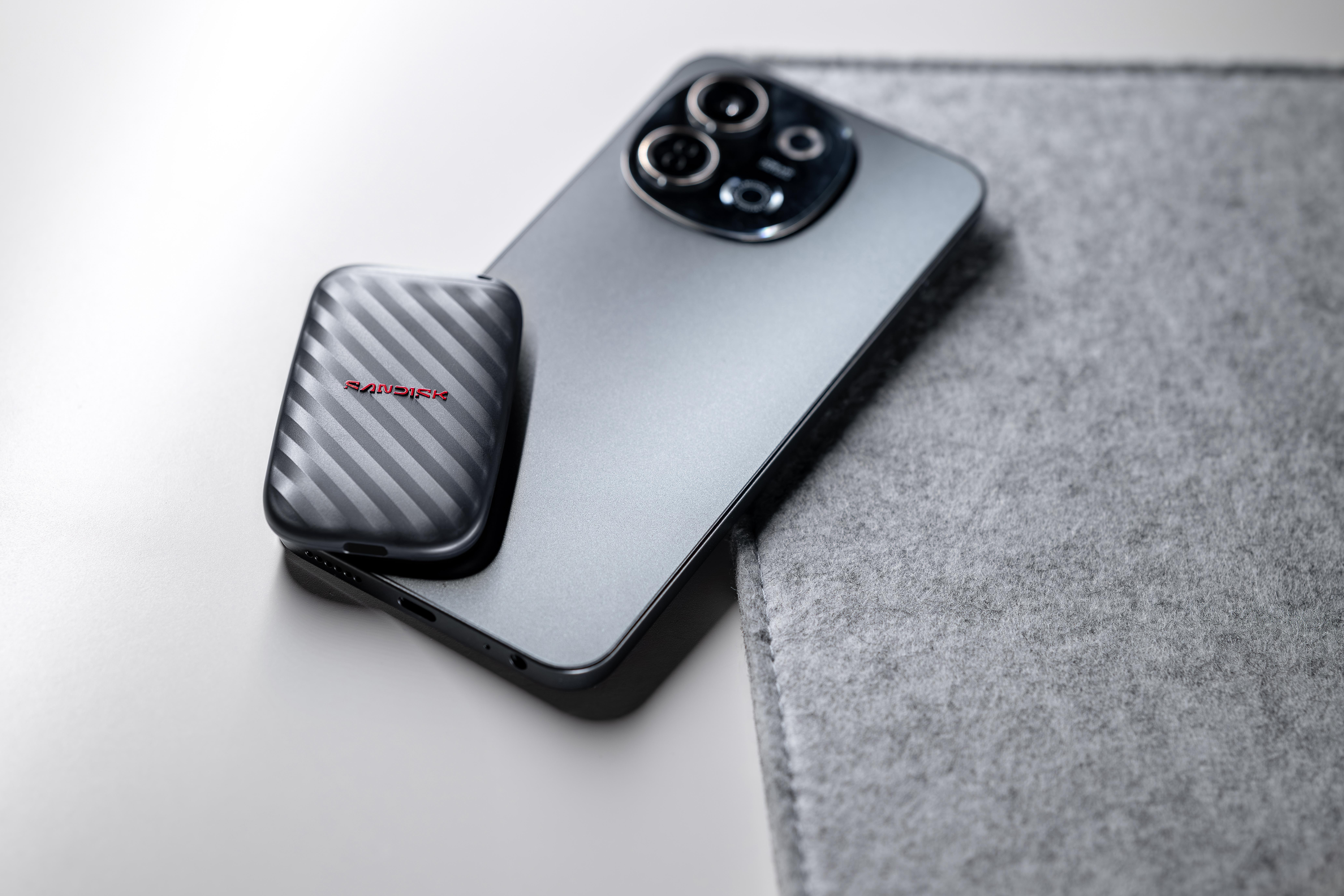 Ein dunkles Smartphone liegt neben einer grauen Filzmatte, mit einer SanDisk SSD darauf.