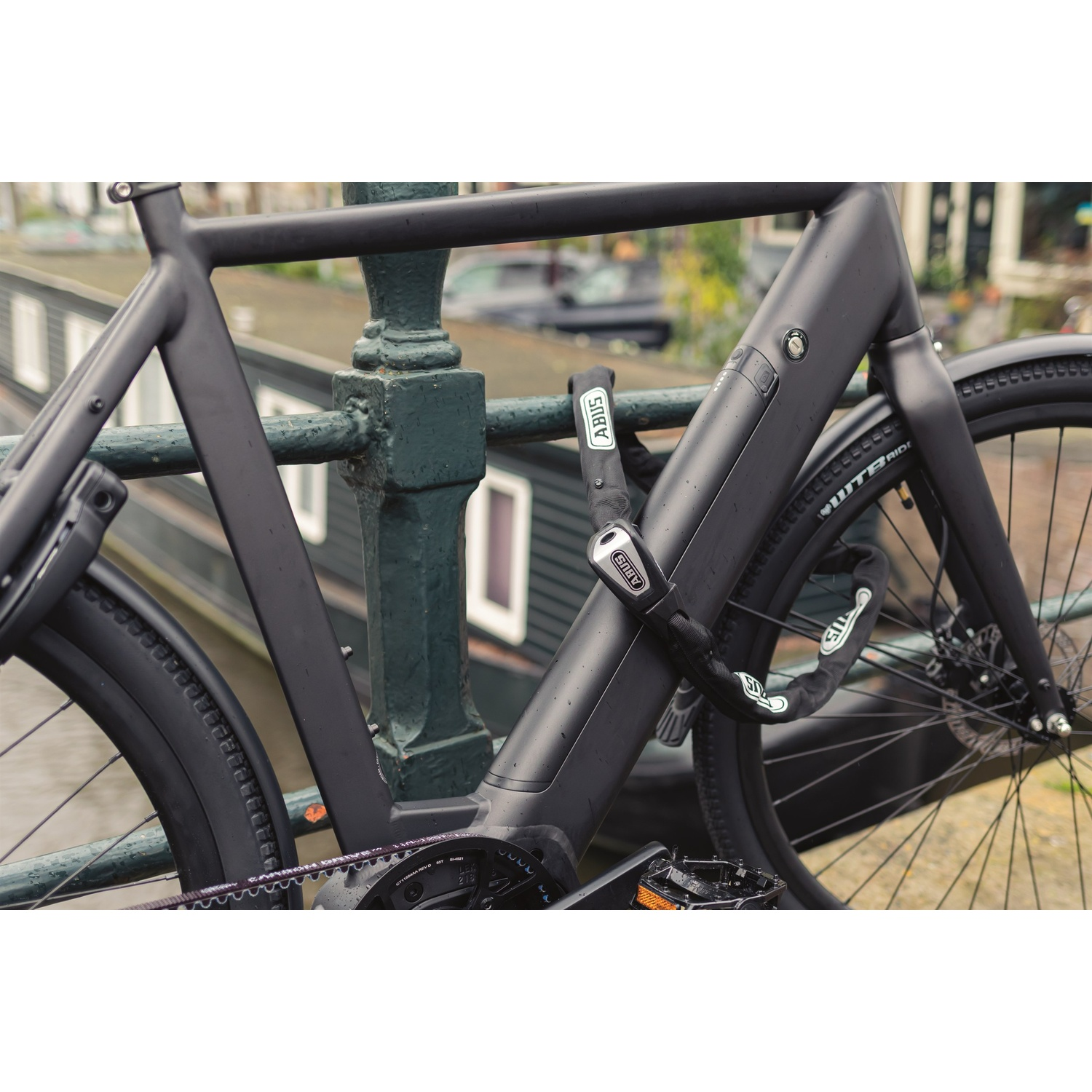A matte black electric bicycle is secured to a bridge railing with an ABUS chain lock.
