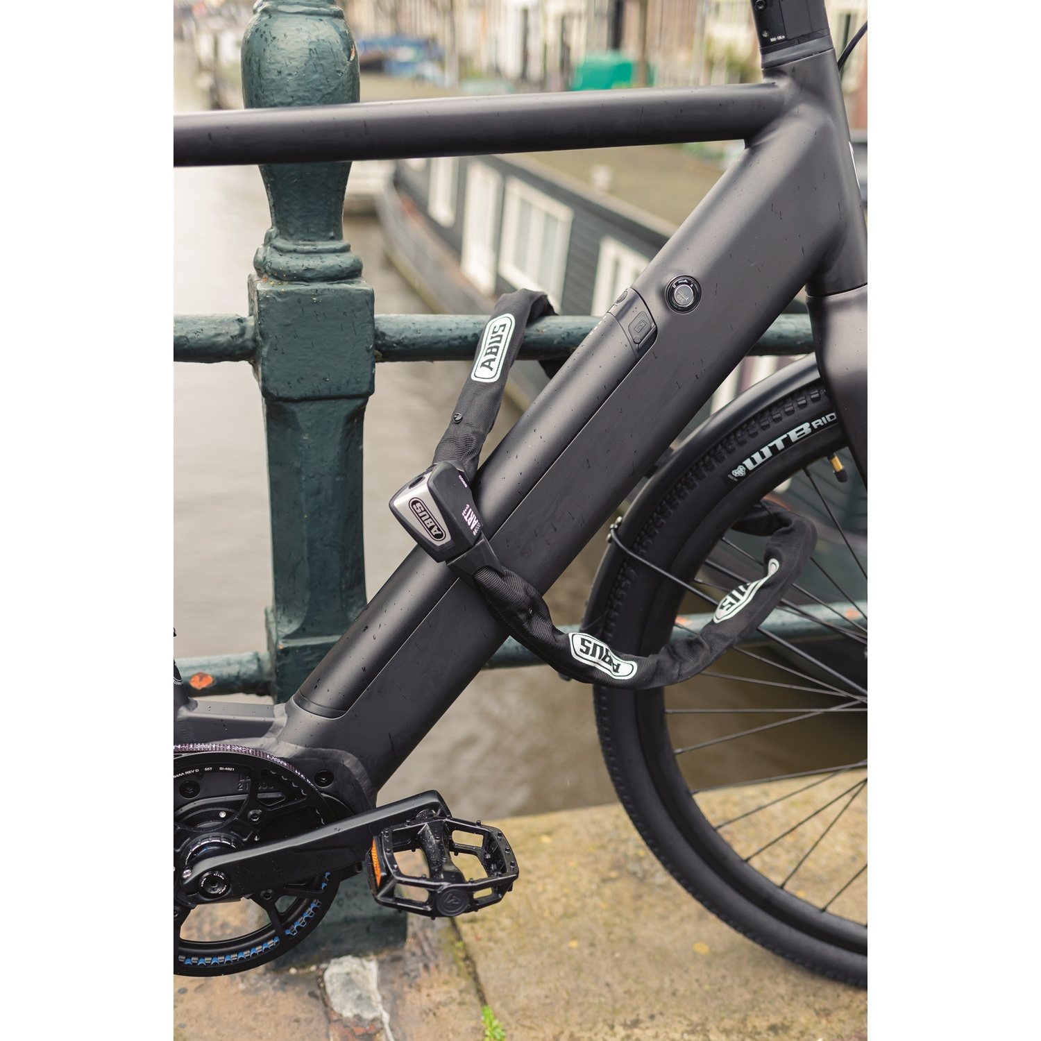 A matte black electric bicycle is secured to a bridge railing with an ABUS chain lock.