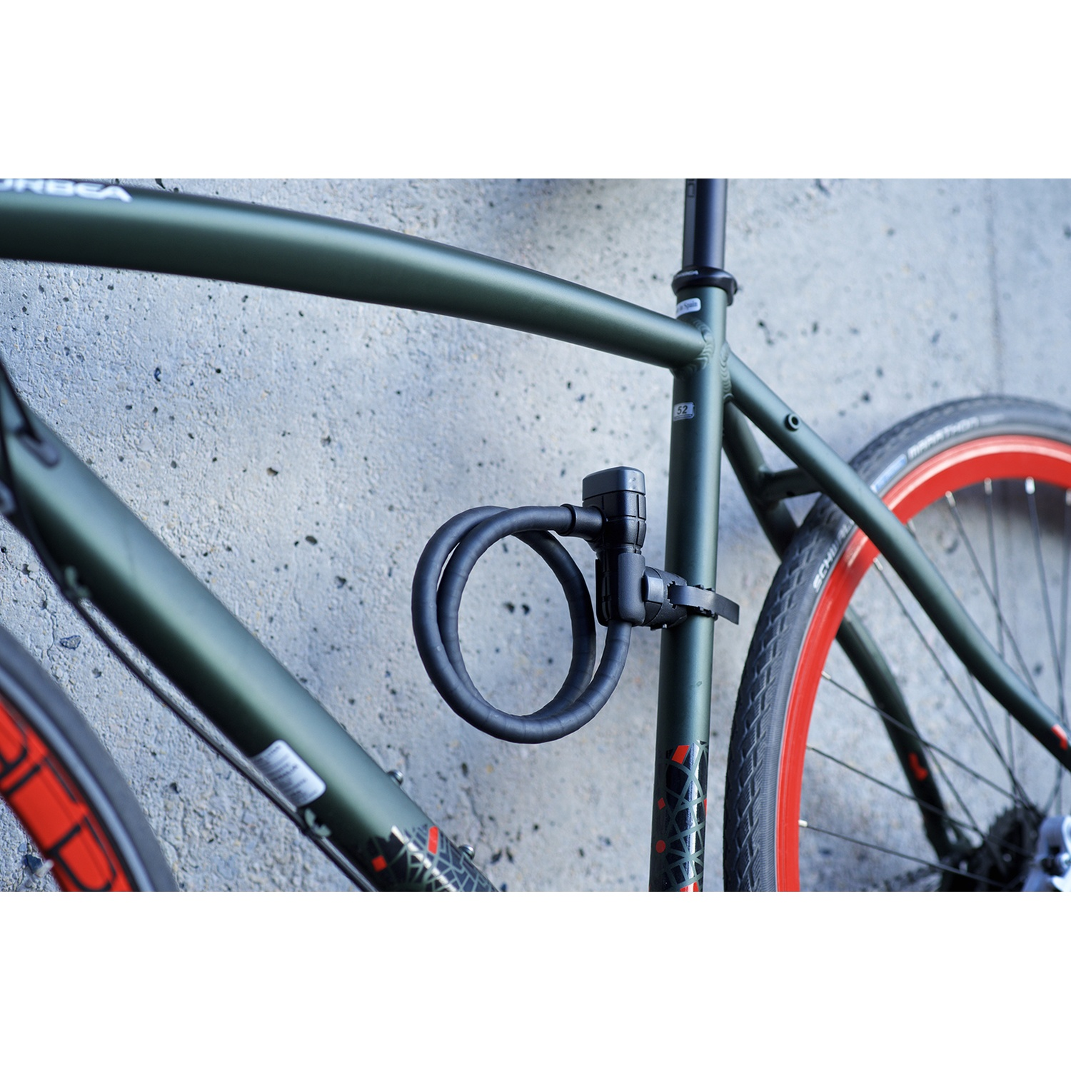 A green bicycle with red rims and a black coiled cable bike lock mounted on the frame.