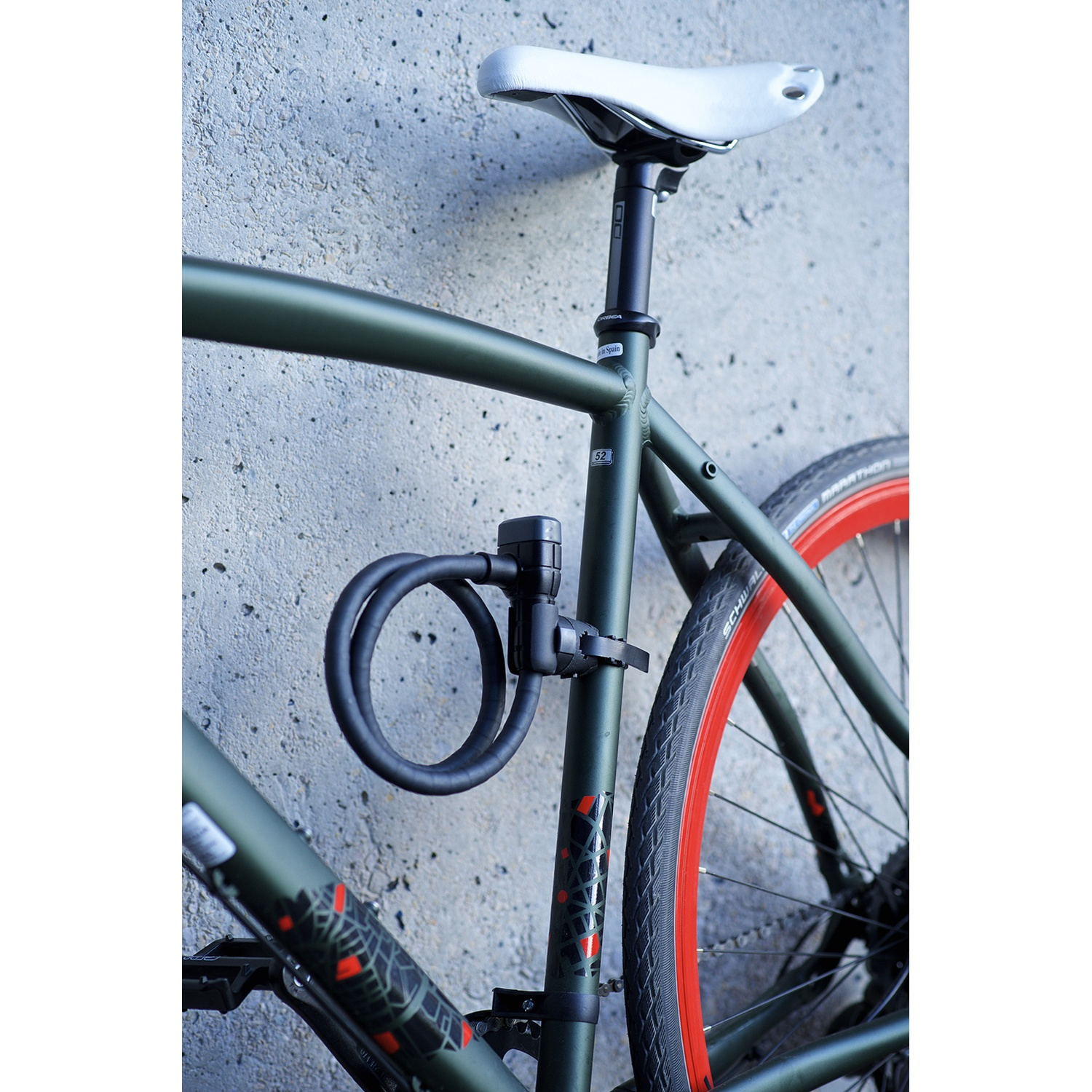 A green bicycle with a black U-lock and white saddle, parked in front of a gray concrete wall.