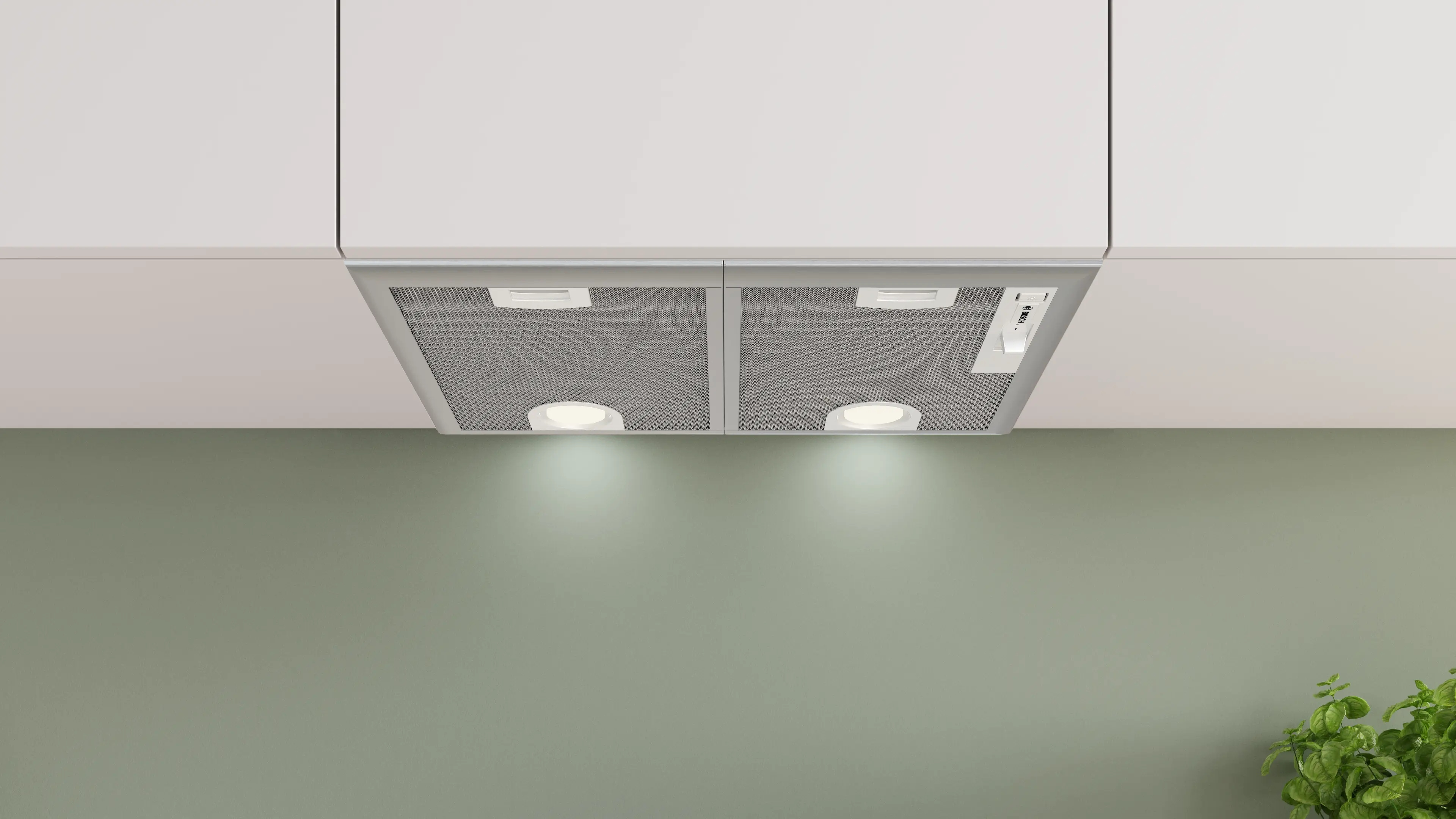Campana extractora bajo mueble con filtros metálicos y dos luces redondas encendidas bajo armarios blancos.