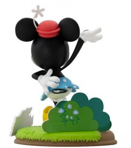 Rückansicht einer Minnie-Mouse-Figur im blauen Polka-Dot-Rock, die hinter grünen Büschen auf einer Wiese steht.