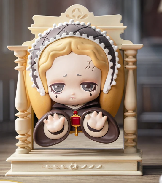 Eine melancholische Figurine mit dunkler Haube und Händen in einem beigen Rahmen.
