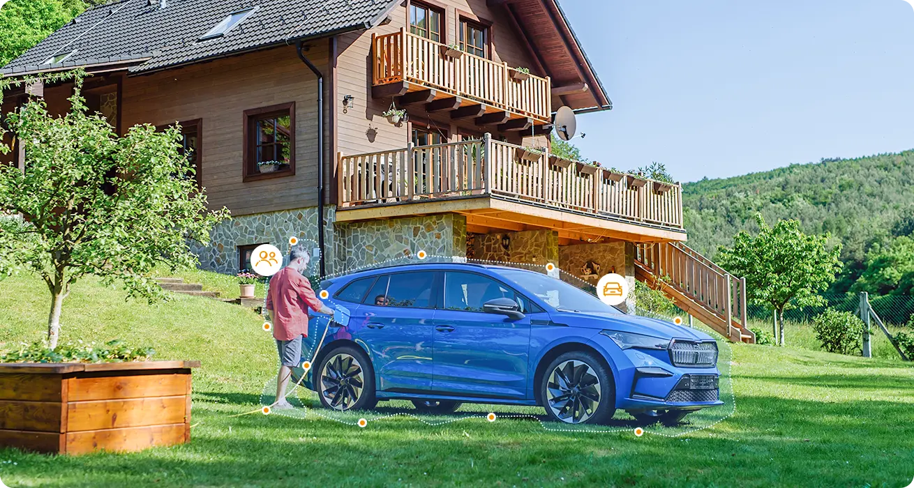 Egy férfi kék elektromos autót tölt egy nagy faház előtti füves udvaron.