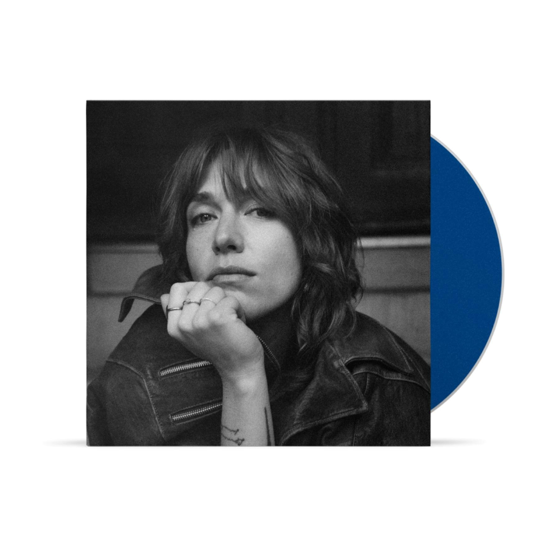 Schwarz-Weiß-Porträt einer Frau in einer Lederjacke, gestützt auf ihre Hand, mit einer blauen Vinylplatte im Hintergrund.