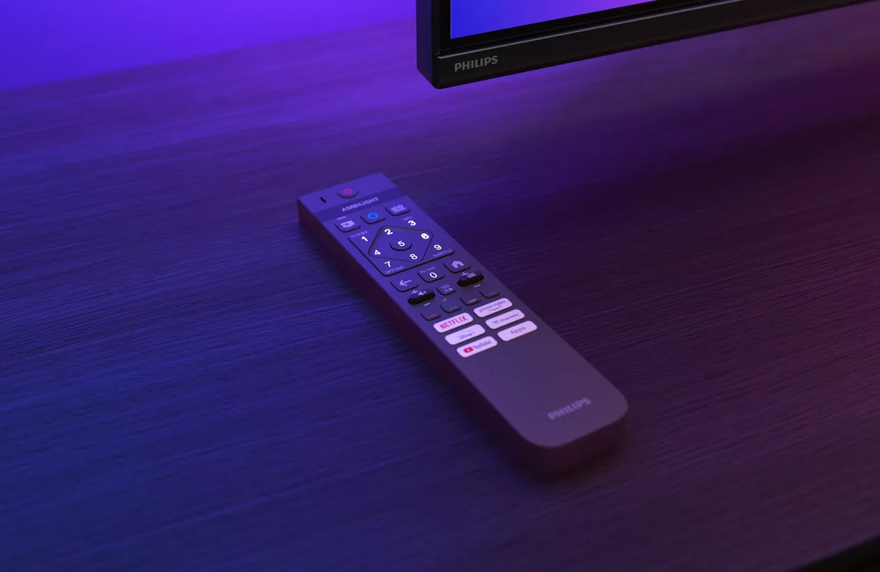 Pilot do telewizora Philips leży na ciemnej drewnianej powierzchni w fioletowym świetle.