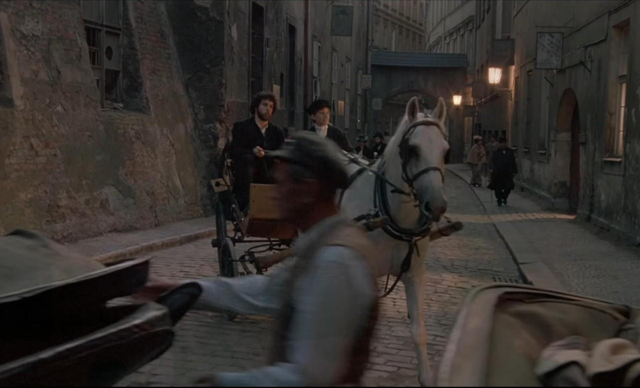 Ein weißes Pferd zieht eine Kutsche durch eine enge Kopfsteinpflasterstraße mit historischen Gebäuden.