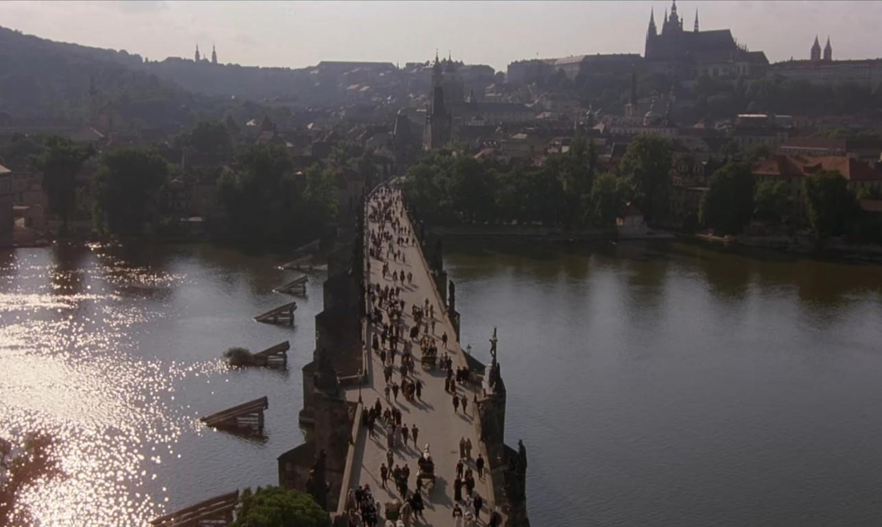 Eine lange Brücke mit vielen Fußgängern überquert einen Fluss, im Hintergrund ist eine Stadt zu sehen.
