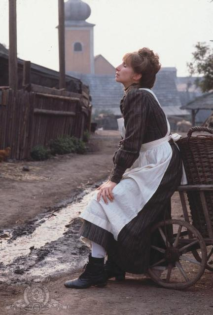 Eine Frau in historischen Kleidern sitzt auf einem Karren in einem ländlichen Dorf.