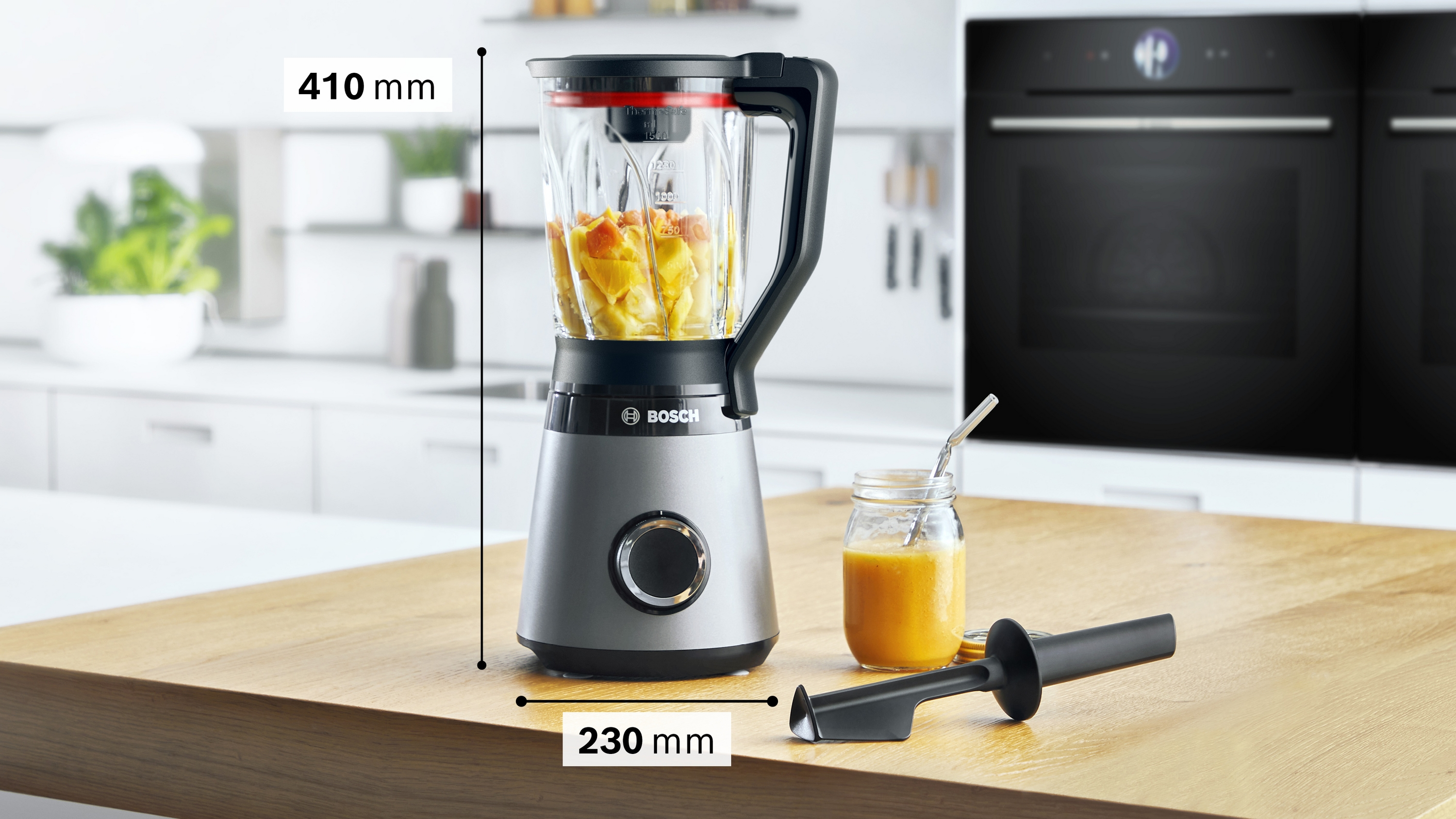 Grauer Bosch-Standmixer auf Holztisch, daneben ein Glas Smoothie und ein Spatel in moderner Küche.