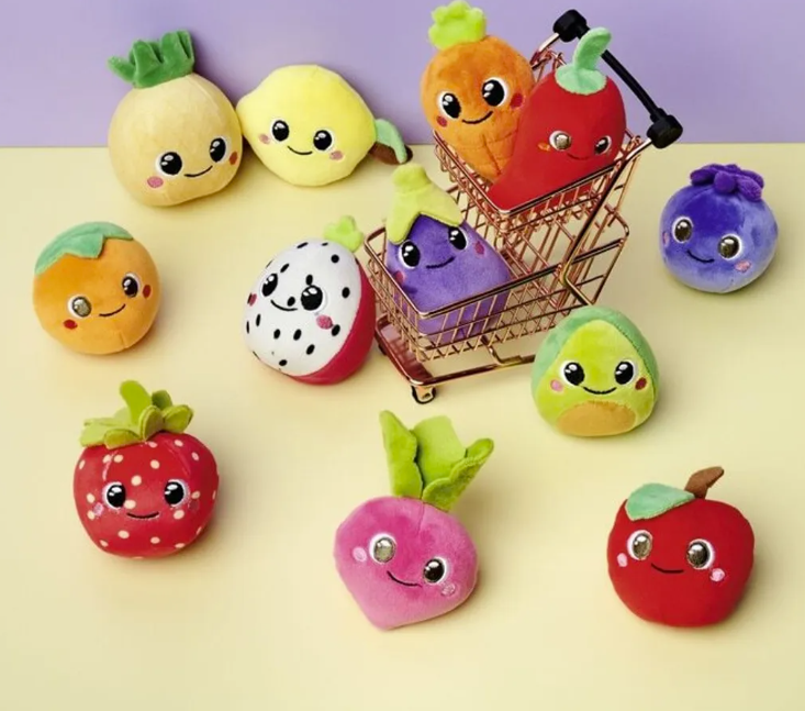 Niedliche Plüschtiere in Frucht- und Gemüseform liegen um einen kleinen Einkaufswagen.