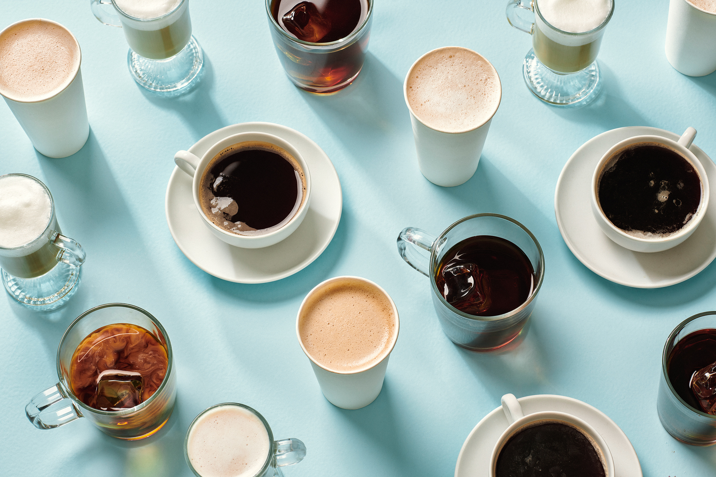 Verschiedene Kaffee- und Getränkebecher in Mustern auf hellblauem Hintergrund angeordnet.