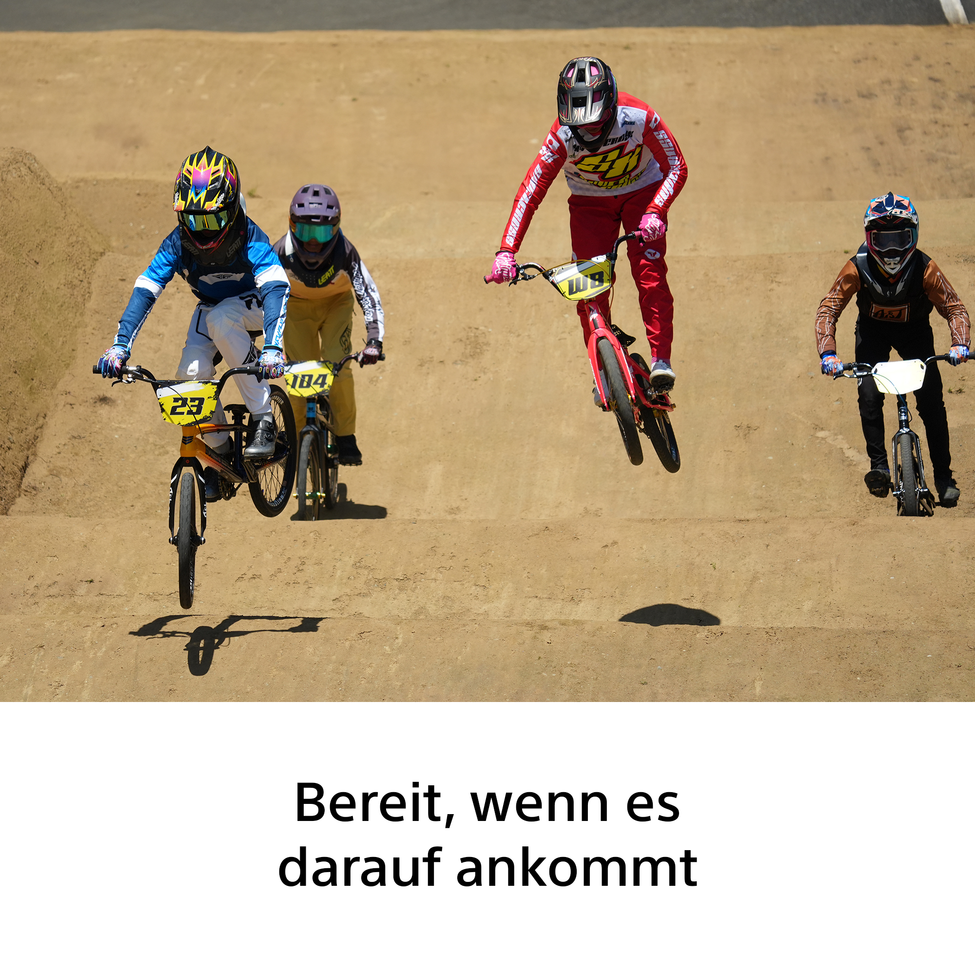 Vier BMX-Fahrer in Schutzkleidung springen mit ihren Fahrrädern auf einer Sandbahn, während ein Text unten zu sehen ist.