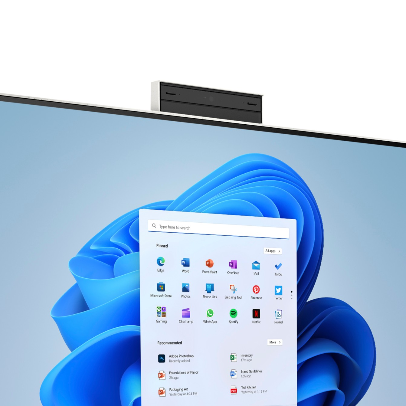 Una pantalla de ordenador muestra el menú de inicio de Windows 11 sobre un fondo azul, con una cámara web arriba.