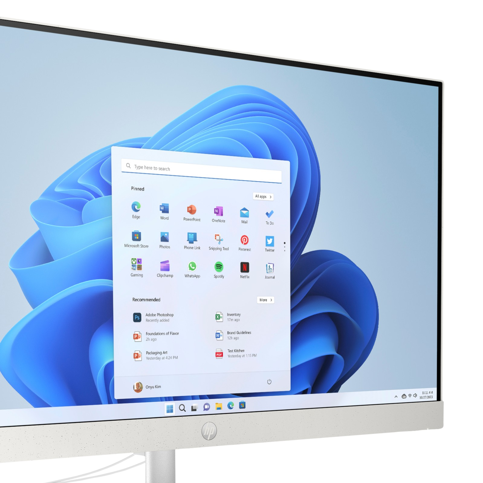 Un monitor de computadora muestra el menú de inicio de Windows 11 sobre un fondo azul abstracto.