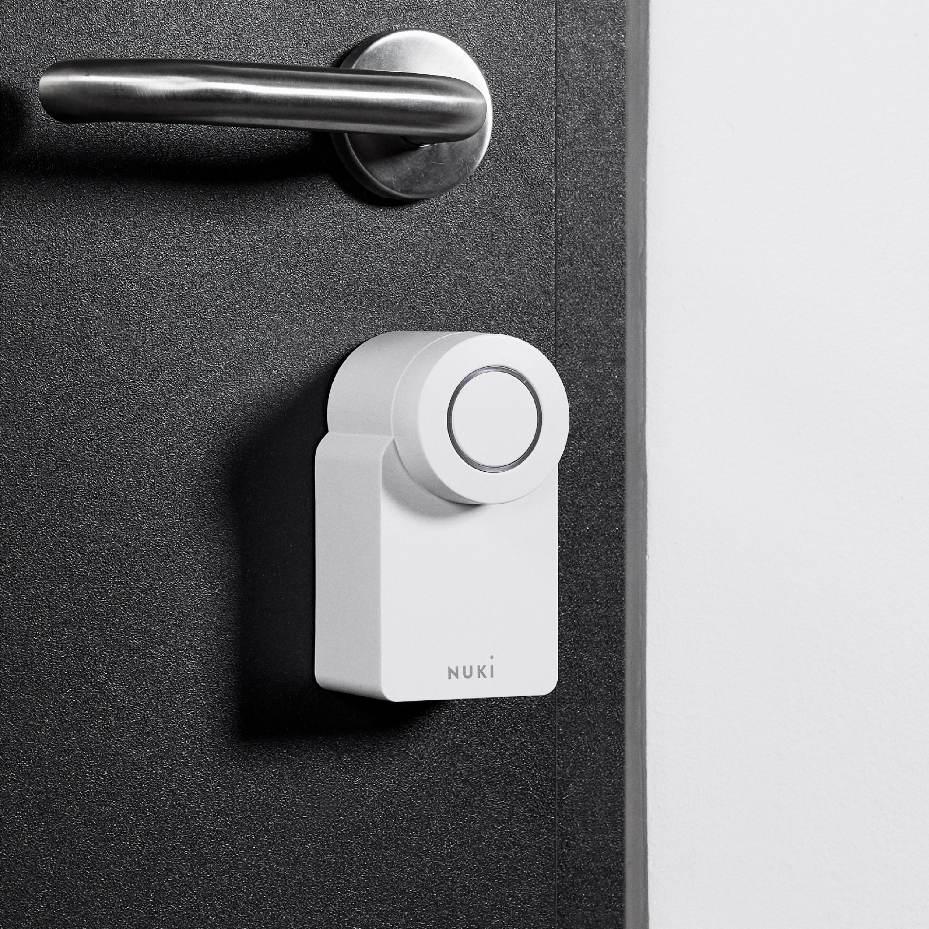 Ein weißes Nuki Smart Lock ist an einer dunklen Tür unter dem Türgriff montiert.