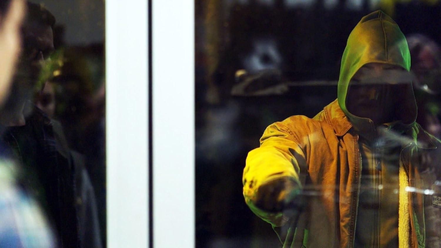 Eine Person im gelben Kapuzenpulli greift vor einem Fenster, während andere Personen zuschauen.