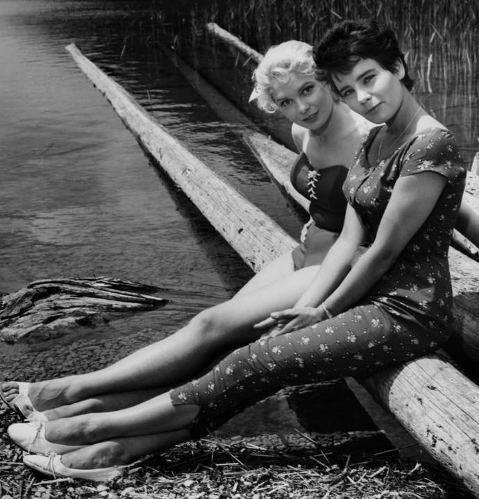 Zwei Frauen sitzen im Freien auf Baumstämmen am Wasser und posieren.