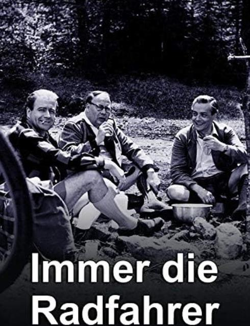 Drei Männer sitzen im Freien auf dem Boden und trinken, mit dem Text "Immer die Radfahrer" unten.