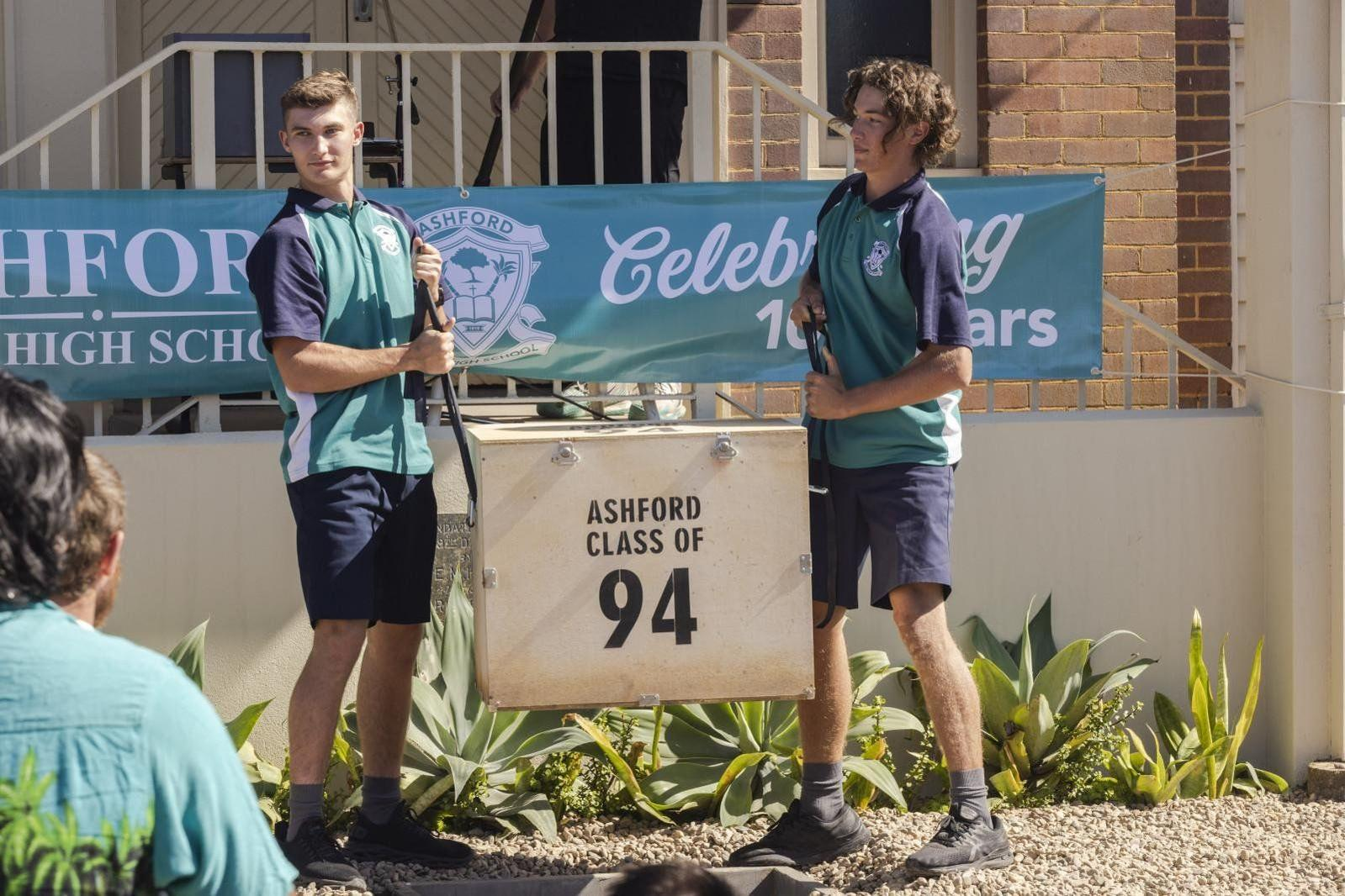 Zwei Jungen in Schuluniform halten Seile einer Zeitkapsel mit Aufschrift Ashford Class of 94.